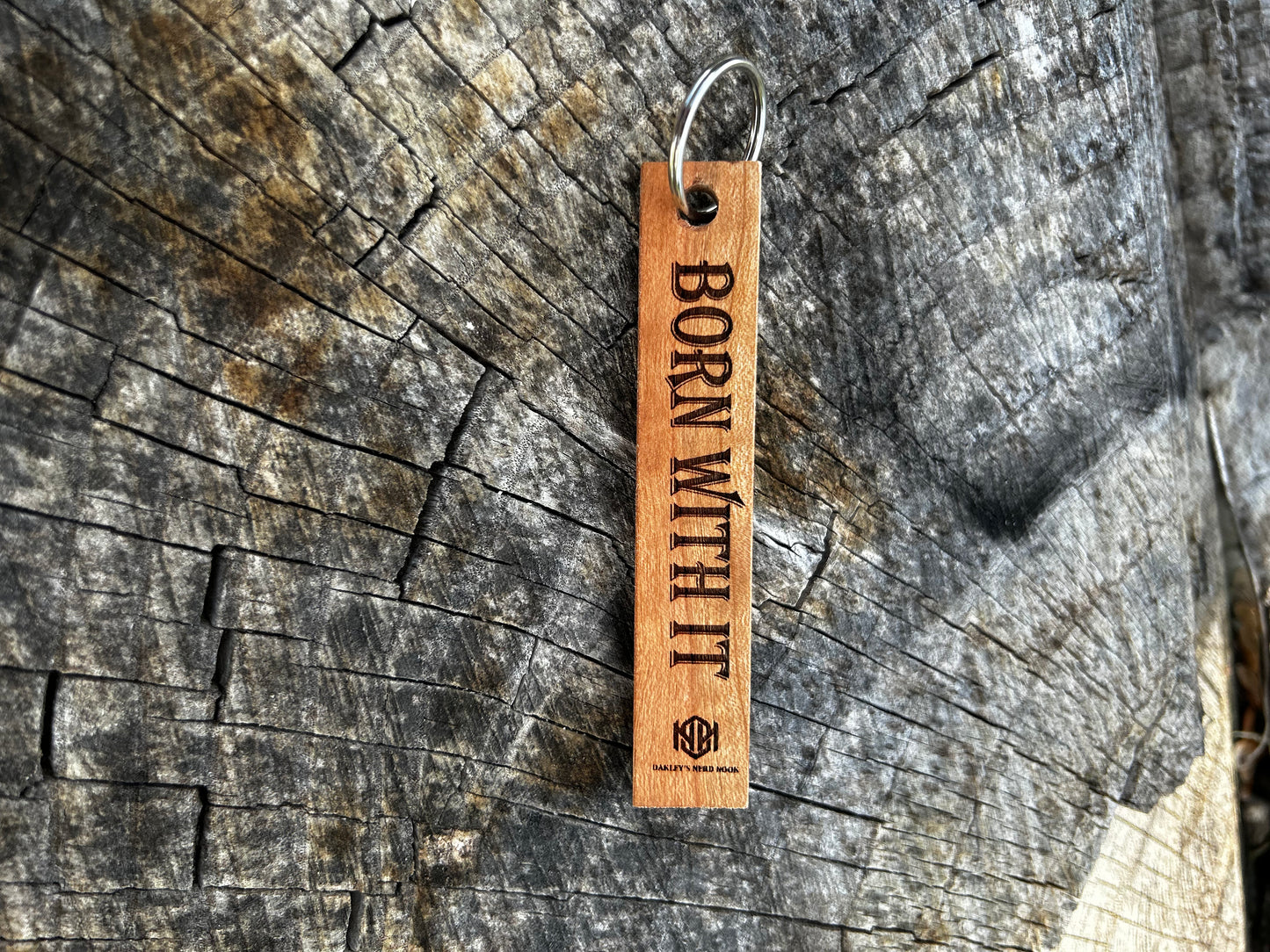 Cherry Wooden Keychain with the words "Born With It" and the Oakley Nerd Nook logo pressed into it