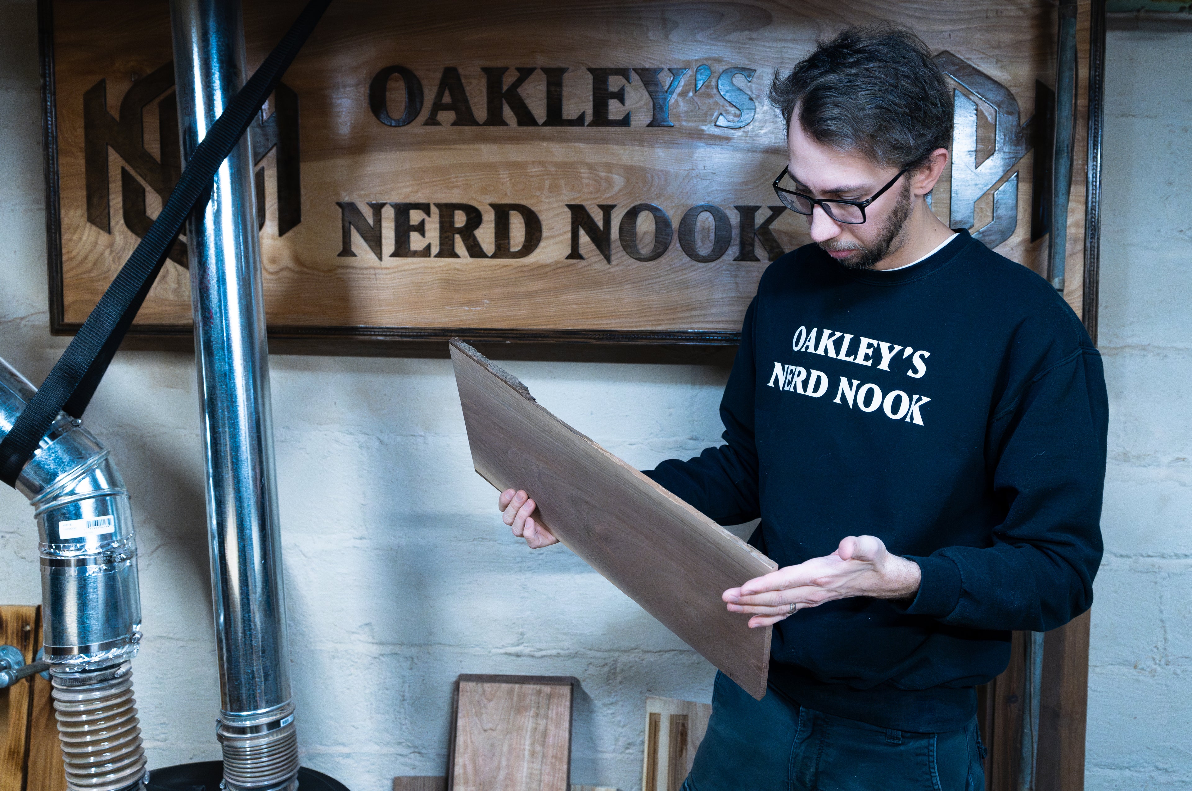 Portrait of Oakley Lyon holding a wooden plank standing in front of a sign that says "Oakley's Nerd Nook"