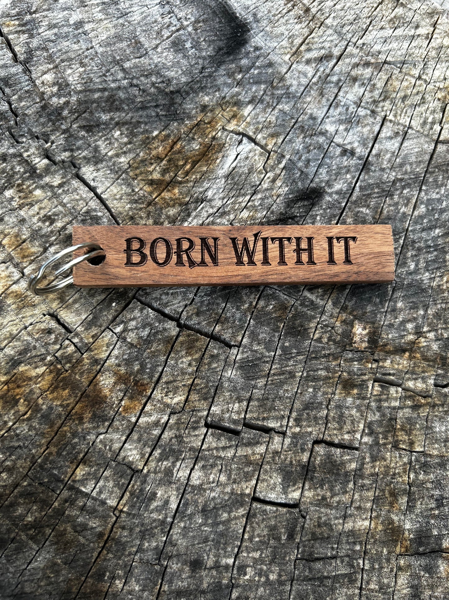 Walnut Wooden Keychain with the word "Born With It" and the Oakley Nerd Nook logo pressed into it